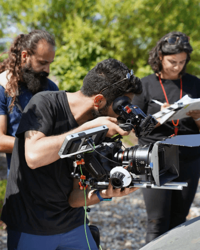 Man filming man under dappled green sunlight.